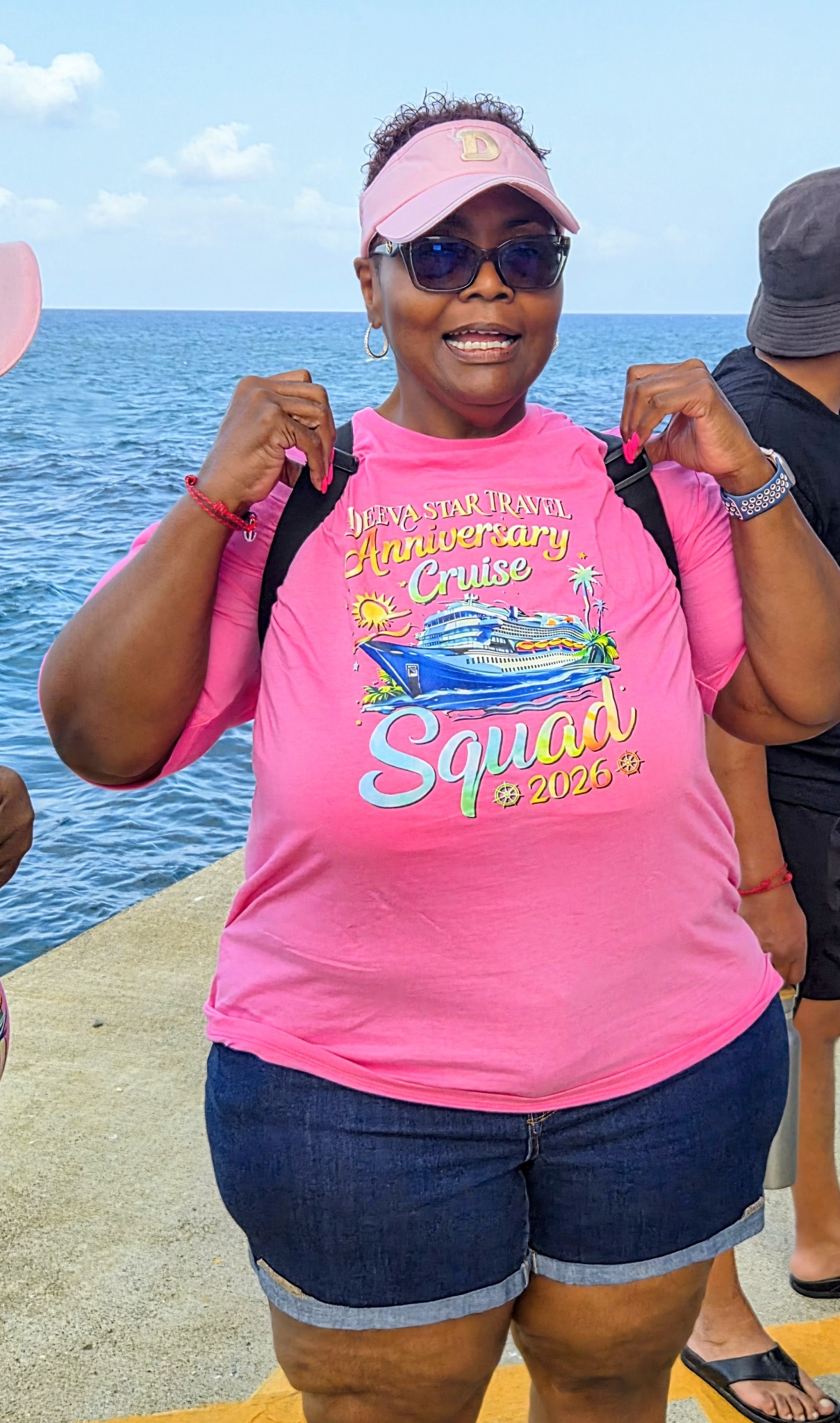 Deanna Moore by the sea in her pink Deeva Star Travel anniversary cruise shirt